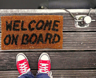 Eine Fußmatte mit der Aufschrift Welcome on Board befindet sich auf der Reling eines Schiffes und begrüßt unsere neuen Mitarbeiter