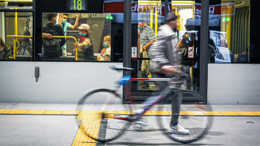 Fahrradfahrer fährt im Vordergrund einer Ubahn. Das Fahrrad sowie der Fahrer sind verschwommen, um Geschwindigkeit darzustellen